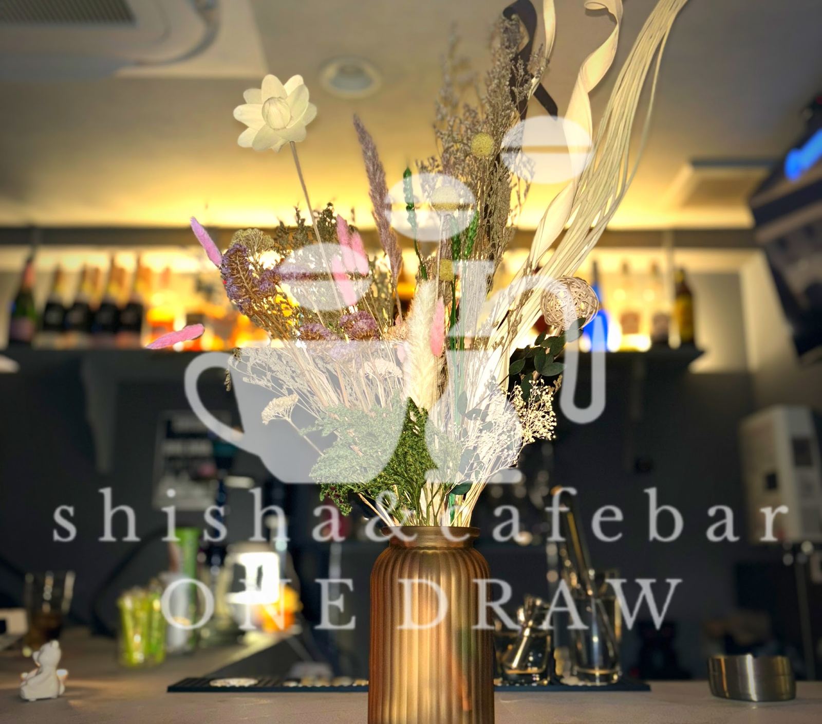 ONE DRAWの店内。カウンター奥のボトル棚が琥珀色に灯り、ドライフラワーが飾られている
